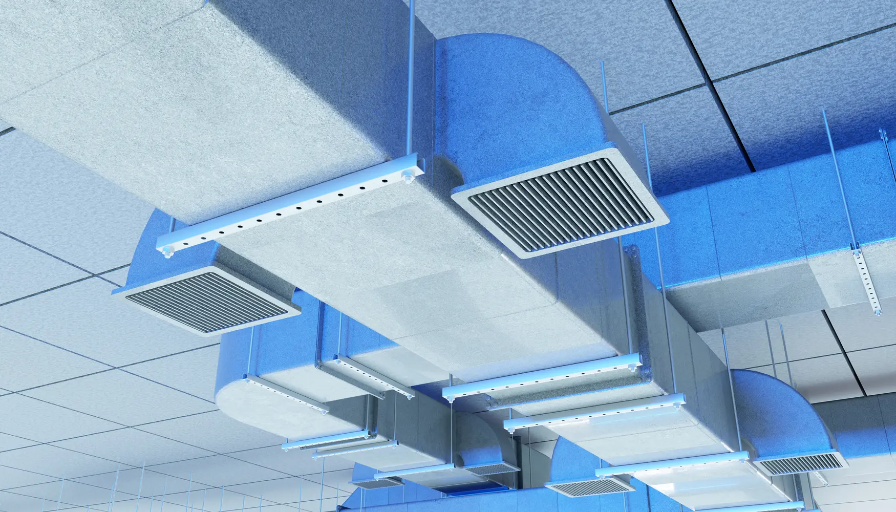 Mehrere blaue Lüftungsschächte verlaufen unter einer Rasterdecke mit Gitterabdeckungen